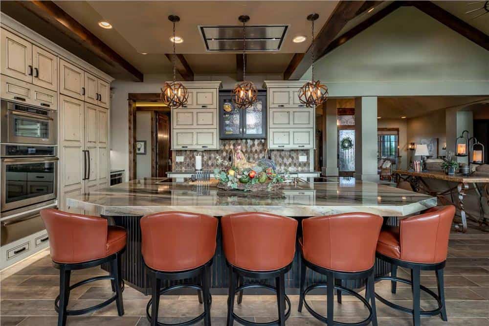 The kitchen is equipped with stainless steel appliances, cream cabinetry, and a center island paired with leather round-back stools.