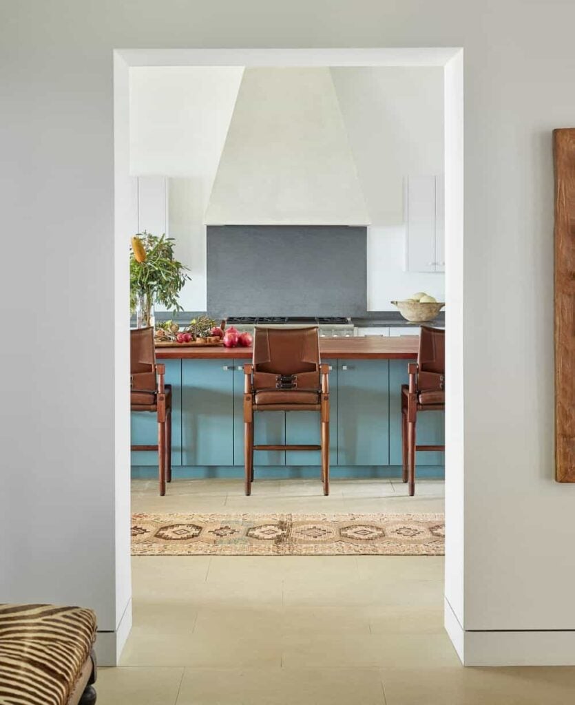 This is a view of the rustic kitchen from the entryway showcasing the large wooden kitchen island with a butcher block counter that matches the wooden stools. On the far side is the cooking area with a large white vent hood.