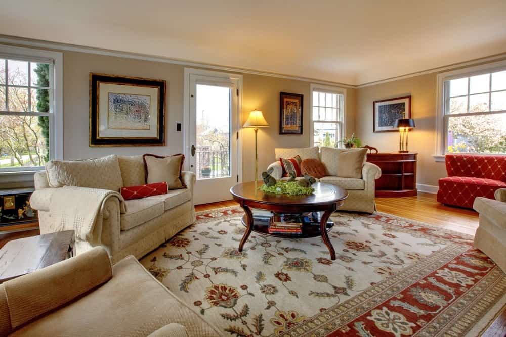 Large living room with beige walls along with red shade. The rug looks classy together with the seats and center table. The warm white lights look so gorgeous.