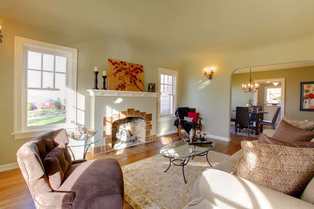 This living room offers beige walls lighted by wall lights. There's a fireplace near the sofa set on top of a classy rug.