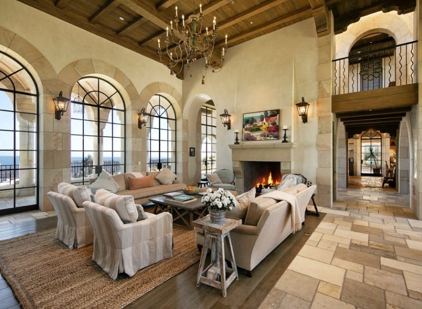 Large Mediterranean living room featuring stunning tiles flooring and a high ceiling lighted by a glamorous chandelier. The sofa set looks perfect together with the home's walls.