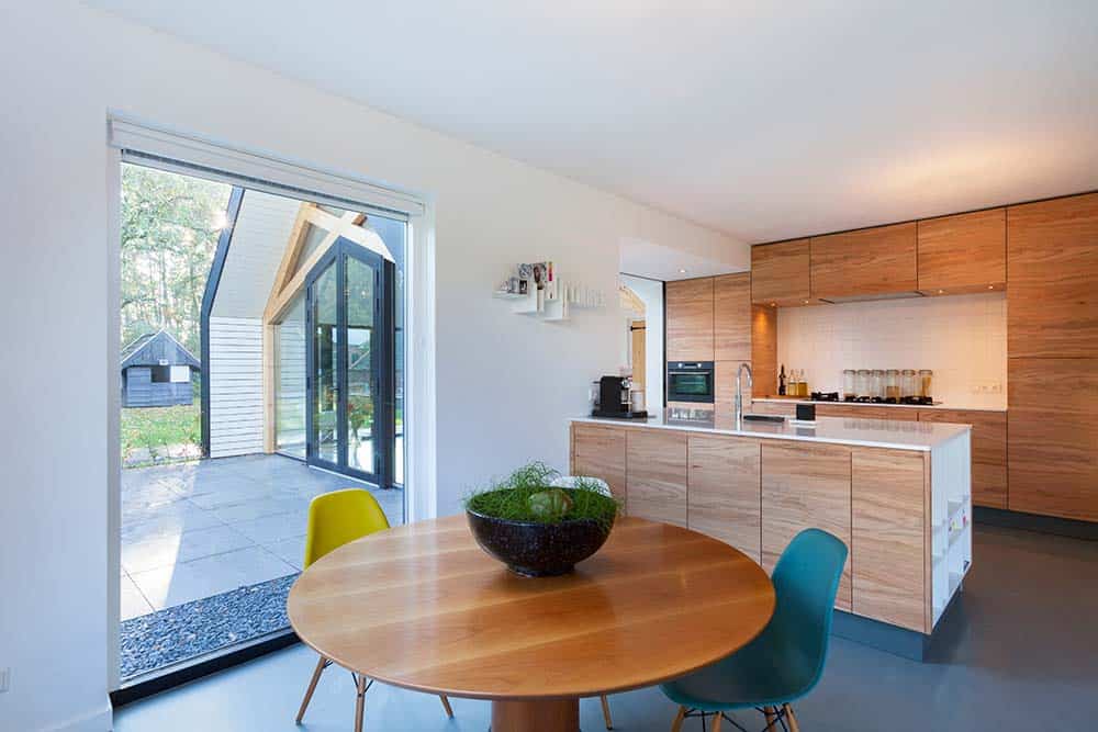 This is a close look at the eat-in kitchen with wooden cabinetry, a wooden peninsula and a wooden dining set that has a round table paired with modern chairs.