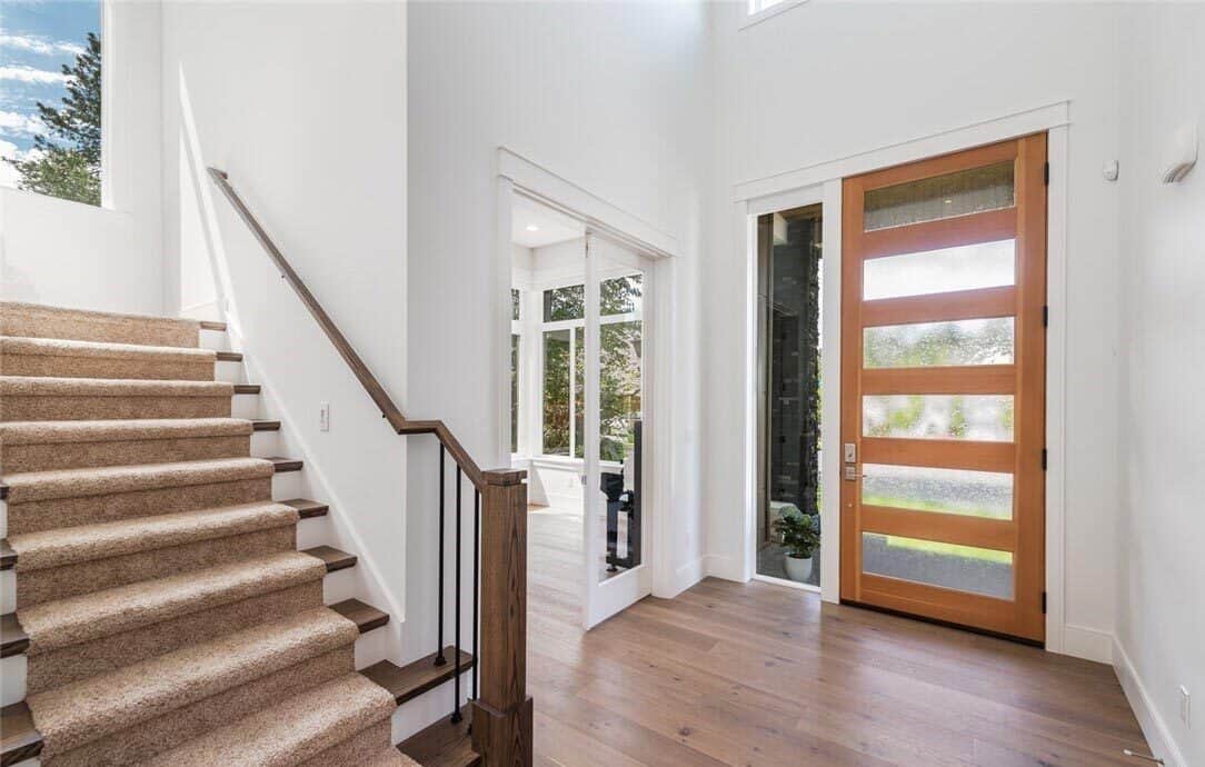 Foyer with wide plank flooring and a staircase dressed in a beige carpet.