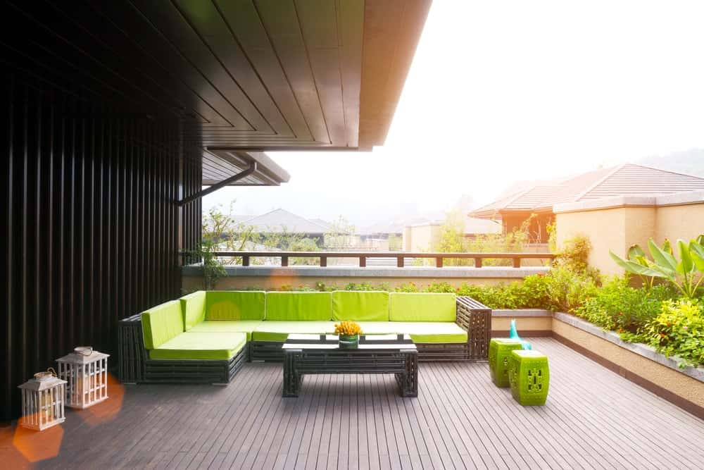 This deck offers a long L-shape outdoor sofa set with green seats and backrests matching the surrounding green plants.