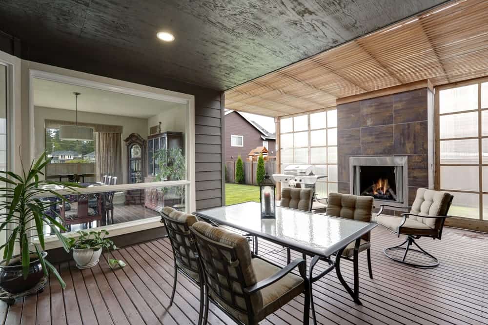 Modern covered deck with a small dining table set and a fireplace.