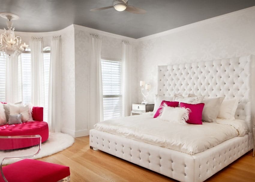 This girl's bedroom offers a classy queen-sized bed with a large headboard matching the elegantly-designed white walls. The seats add color to the room.