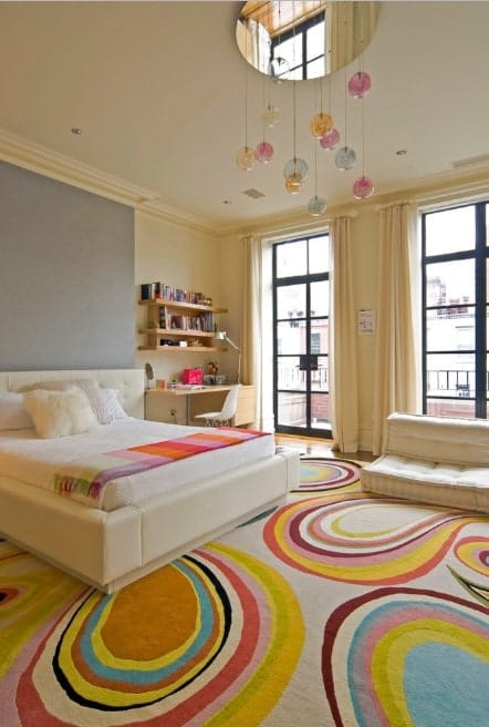 Large girl's bedroom with classy floor rug along with beige walls and window curtains. The bed and the desk are perfectly placed.