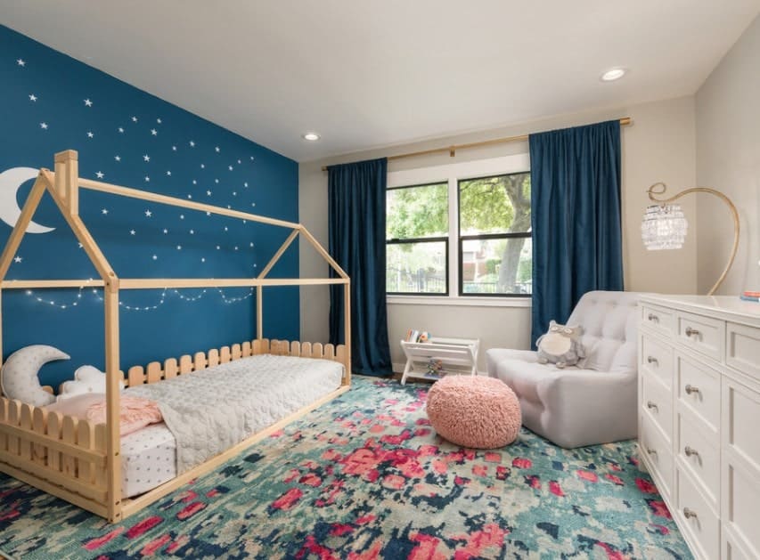 This girl's bedroom boasts a lovely blue wall with very charming stars and moon designs. The blue window curtains match well with the blue wall and rug.