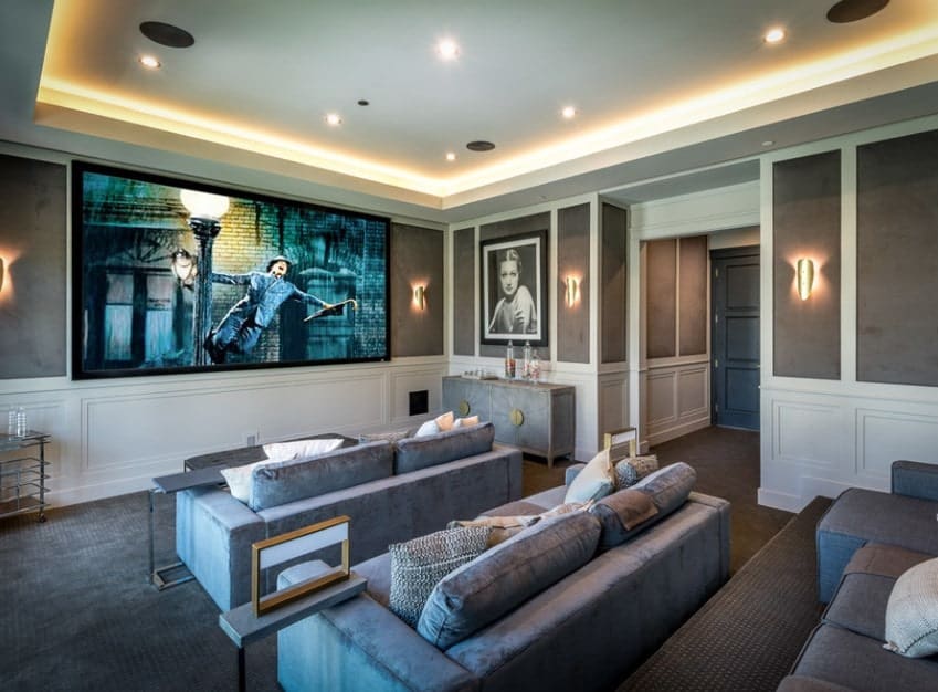This home features a home theater with classy walls and stunning ceiling along with gray carpet flooring matching the gray sectional seats.