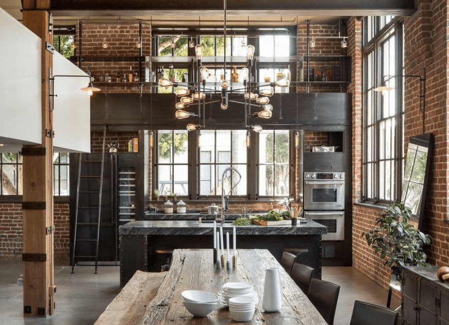 Large industrial kitchen with brick walls and stylish countertops on both kitchen counter and center island lighted by a glamorous ceiling light.