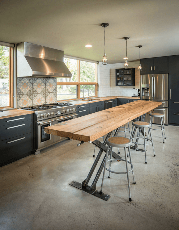 Large industrial kitchen with a breakfast bar made of thick planks lighted by stunning ceiling lights.