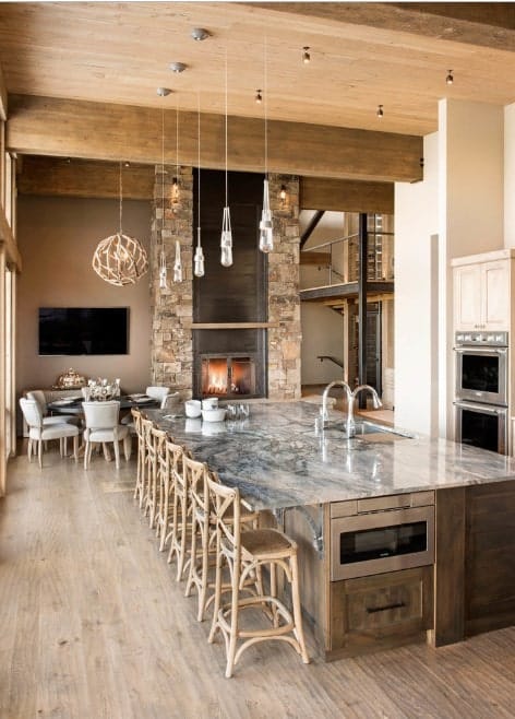 This rustic kitchen boasts a massive center island with stylish marble countertop lighted by pendant lights. There's a brick fireplace too near the dining nook.