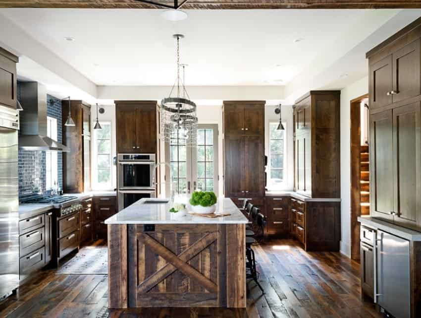 This kitchen features hardwood flooring and rustic cabinetry and center island equipped with a white marble countertop. The ceiling light looks stylish.
