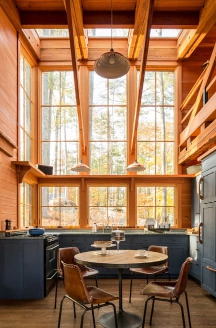 Rustic kitchen with tall ceiling and glass windows. The counters are finished with black adding style to the area. There's a dining nook on the center lighted by pendant lights.