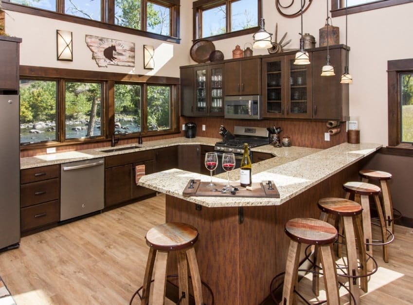 Large kitchen featuring brown finished cabinetry and counters. The marble countertops look glamorous lighted by pendant lights.