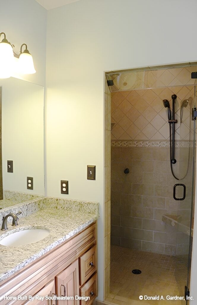 Primary bathroom with wooden vanity and a walk-in shower with corner tiled bench and wrought iron fixtures.