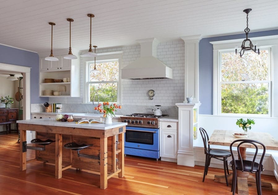 This classy single wall kitchen features lovely hardwood floors and white wooden ceiling lighted by pendant lighting. There's a small dining nook in the corner near the windows.