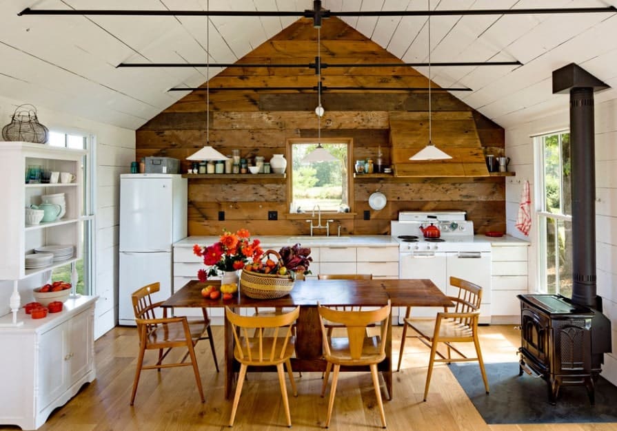 Single wall kitchen with white counter and countertop set on the hardwood flooring that matches the wooden dining table set lighted by pendant lights.