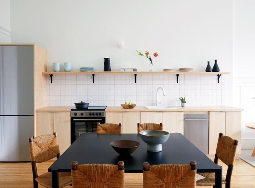 A small single wall kitchen set up with a matte black dining table set in the middle of the hardwood flooring.