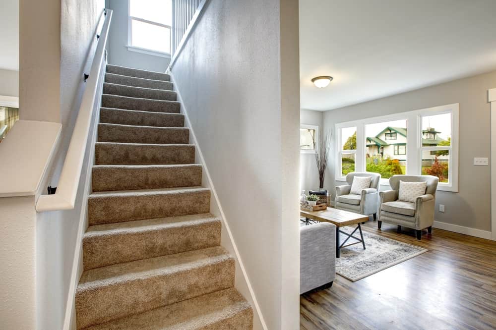 A straight staircase with floors covered with classy carpet. It also features a charming white handrail.