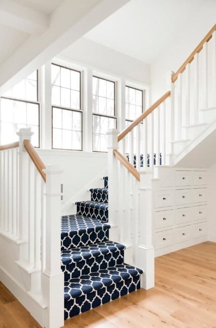 This staircase features stylish carpet floors and white walls, along with white railings and wooden handrails.