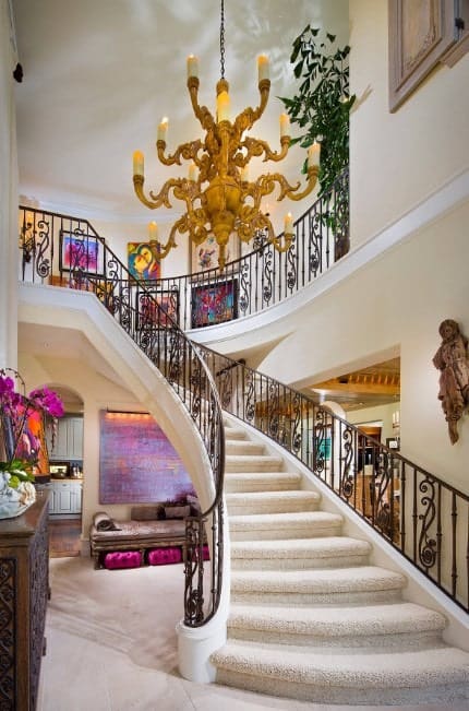 This home boasts a glamorous staircase with white carpet floors and lighted by a stunning chandelier.
