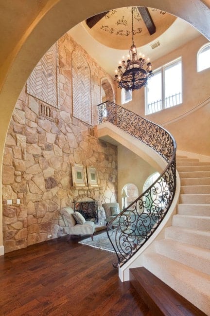 This home boasts a magnificent staircase with white carpet floors and stylish iron railings lighted by a glamorous chandelier.