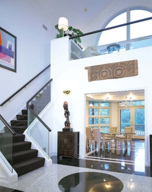 A modern home with a stylish staircase featuring stylish black carpet floors and glass railings.