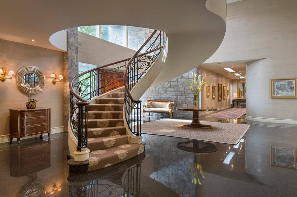 This home's foyer boasts a circular staircase with classy carpet floors and iron railings.
