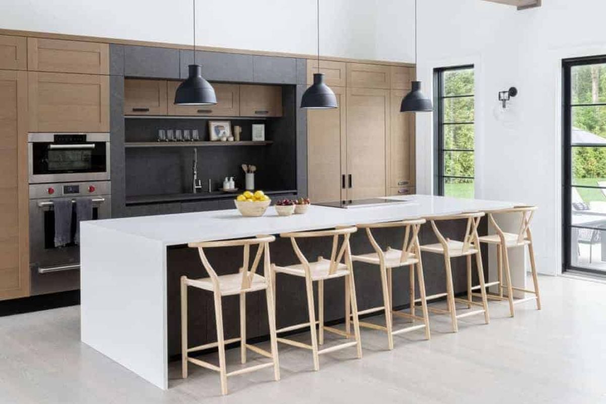 The home features a single wall kitchen with brown cabinetry along with a white breakfast bar countertop lighted by pendant lights.