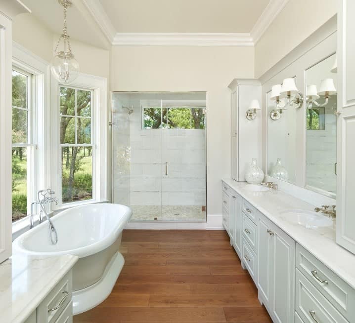 Primary bathroom featuring a double sink with a white marble countertop, a freestanding tub set on the hardwood flooring and a walk-in shower room.