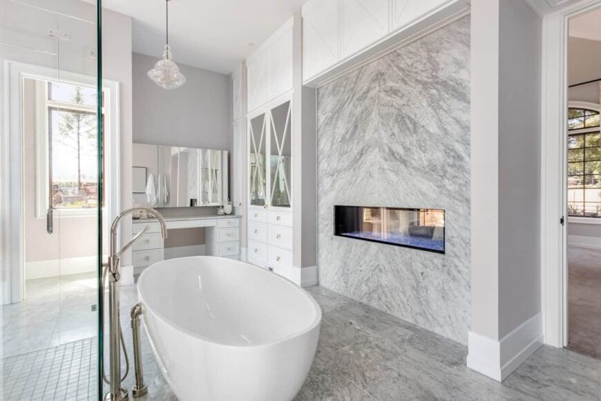 A primary bathroom featuring a white freestanding tub and a fireplace beside it. The room also has a shower area.