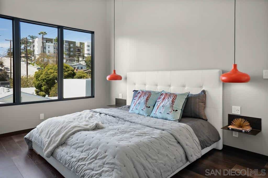 Contemporary master bedroom accented with vibrant orange pendants. It has glass windows overlooking the outdoor scenery.