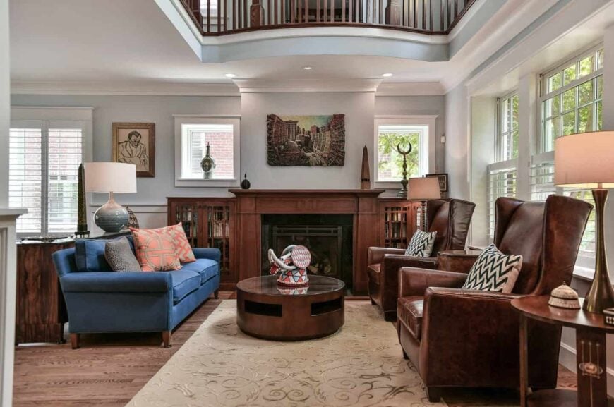 Fresh and light living room accented with blue couch paired with a round wooden table and brown leather high back chairs. 