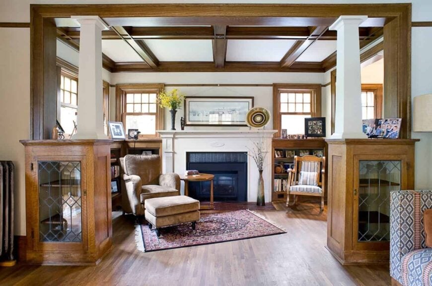 Craftsman living room features a brown velvet recliner that sits on a vintage rug with a wooden round side table beside the fireplace. It also has a hardwood floor along with a coffered wood ceiling.
