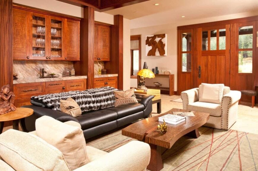 Warm living room with black leather sofa paired with white upholstered chairs and a wooden coffee table. They sit on a line patterned rug over a hardwood flooring.