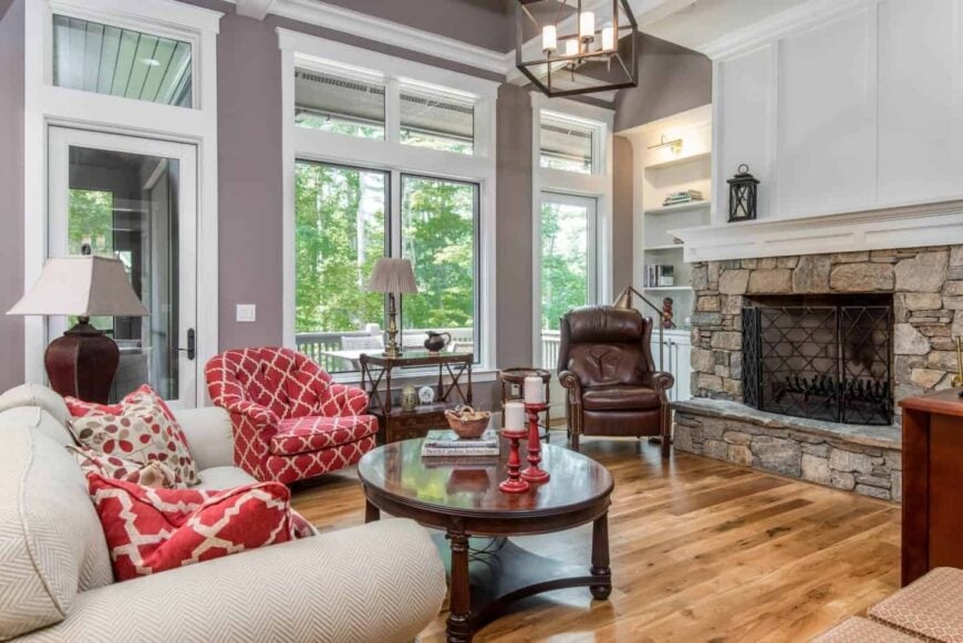 Gorgeous living room with a pop of red from the upholstered chair, throw pillows and candle holders. It features a high ceiling with a hanging cube chandelier.