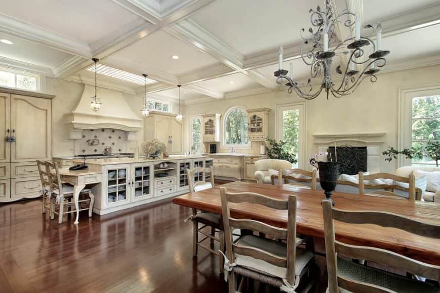 Amazing kitchen with hardwood flooring, white cabinets, rectangular island table with glass cabinets and shelves, two wooden chairs and three fancy pendant lights.