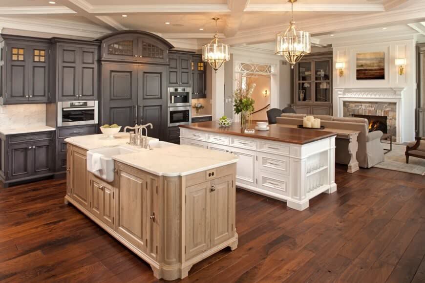 Fabulous kitchen with two wooden island tables, black cabinets, hardwood flooring, stainless steel appliances and two light drum chandeliers hanging on a coffered ceiling.