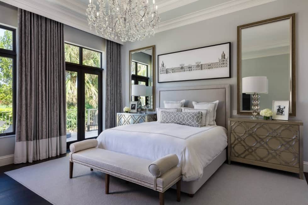 Primary bedroom with a comfy bed set on a rug covering the hardwood flooring. The room is lighted by a stunning chandelier.