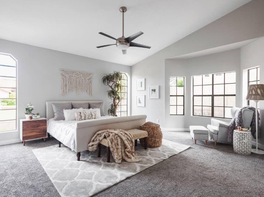 This primary bedroom features light gray walls and carpet flooring topped by a rug.