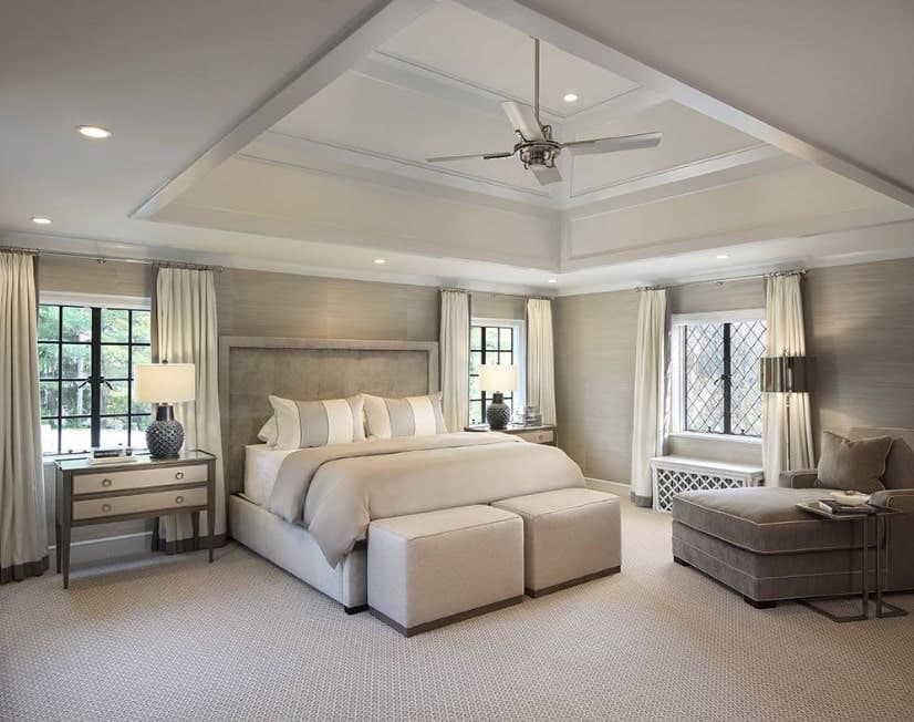 A primary bedroom featuring a classy bed set on the room's carpet flooring and is under the beautiful white tray ceiling.