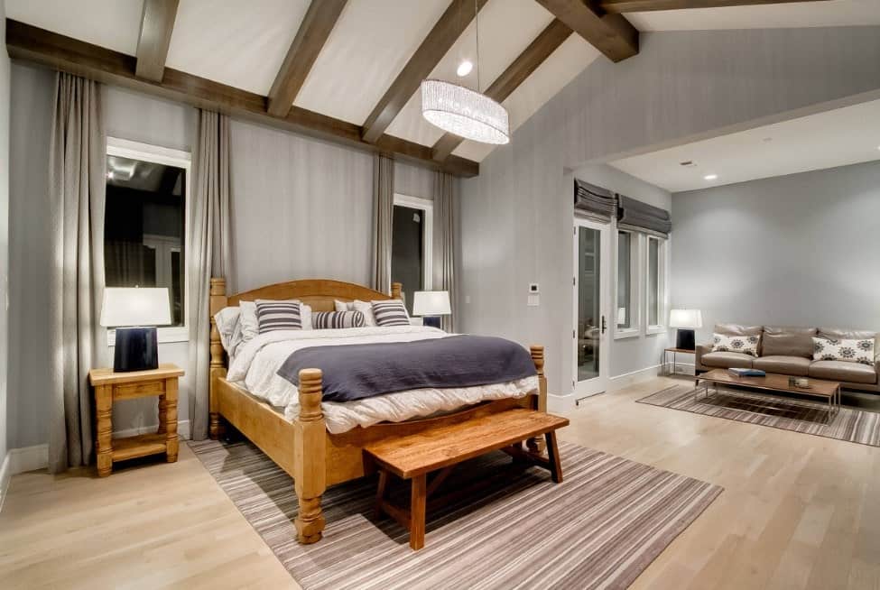 Large primary bedroom with its own living space with a cozy sofa set. The room has gray walls and a vaulted ceiling with exposed beams.