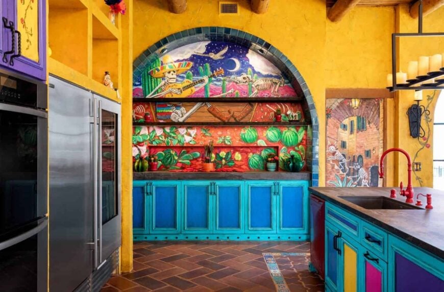 Mexico inspired kitchen accented with an arched mural lined by black brick tiles against the yellow walls. It includes a tiled flooring with herringbone pattern and multi-colored cabinetry.