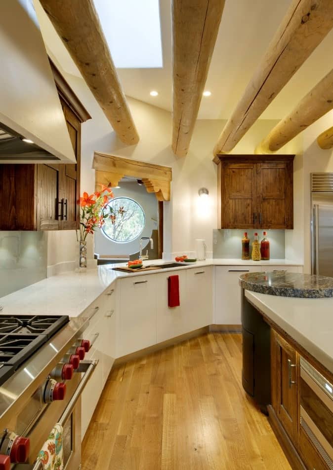 Curved kitchen with dark wood upper cabinetry along with white lower cabinetry. It has huge rounded wood beams and a breakfast island with a circular end.