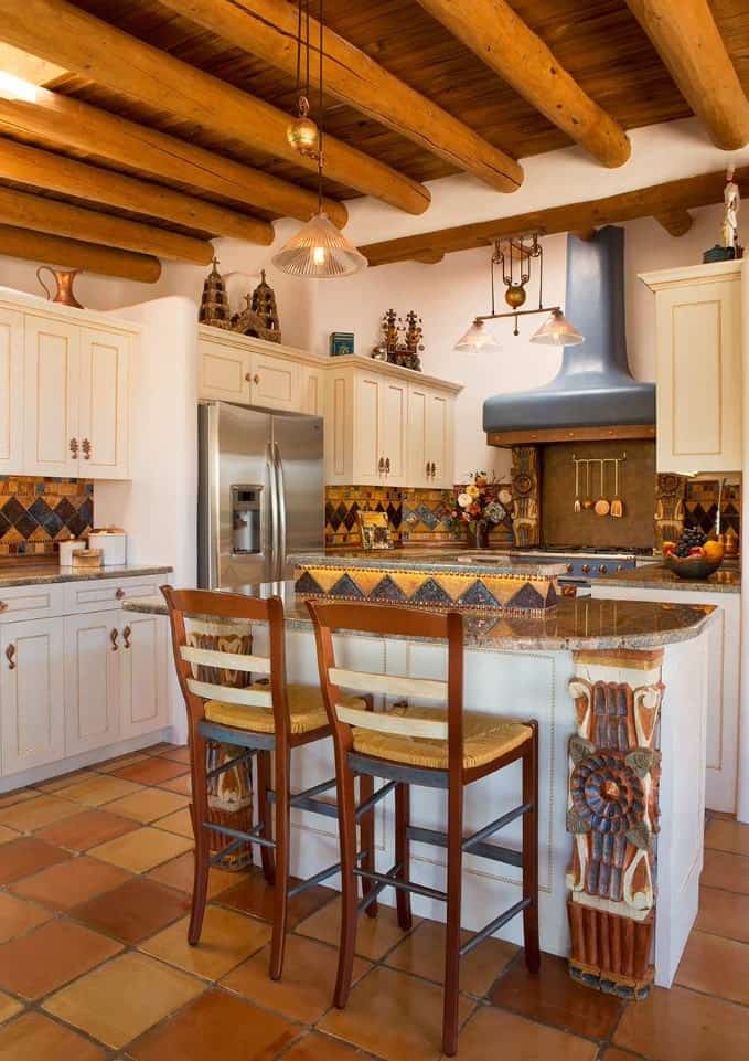 This kitchen features white cabinetry accented with colorful decorative tiles. It has a small breakfast island paired with cushioned counter stools.