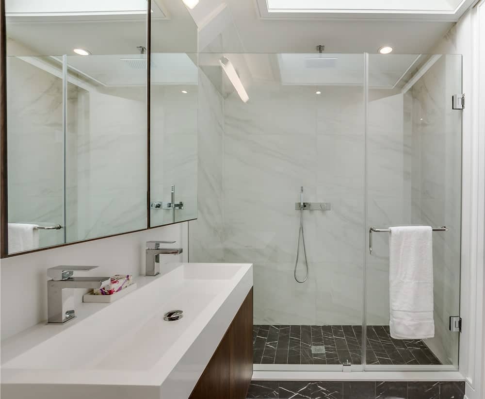 This is the simple bathroom with black flooring tiles, a glass-enclosed shower area on the far side and a floating two-sink vanity on the side.
