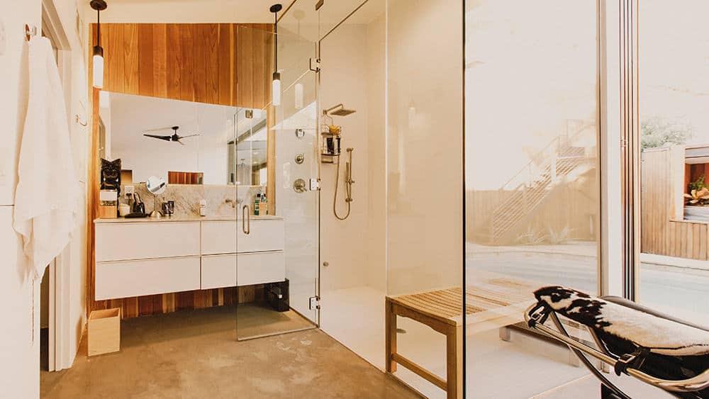 This is a view of the Contemporary-style bathroom with a white floating vanity topped iwth a mirror that matches the glass enclosed shower area on the side of the vanity.