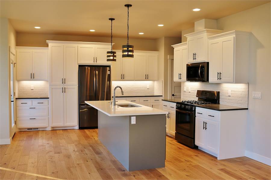The kitchen has hardwood flooring that complements the beige cabinetry contrasted by the dark appliances and gray kitchen island topped with pendant lights.