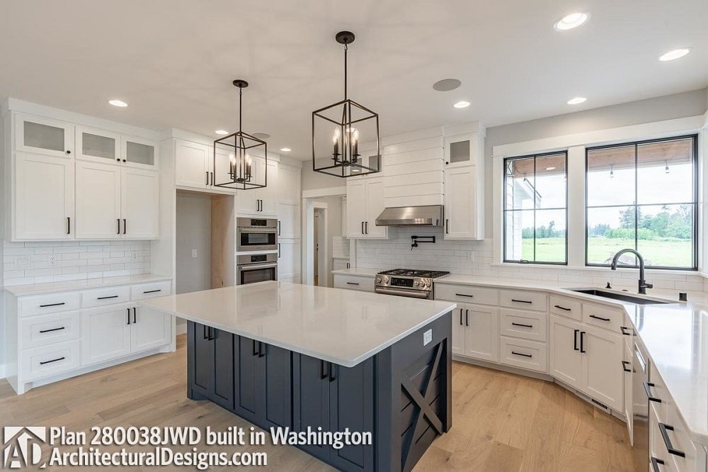The kitchen has a large kitchen island that has a beige countertop to match the surrounding cabinetry along the walls. This is then contrasted by the dark gray island and the wrought-iron pendant lights above.
